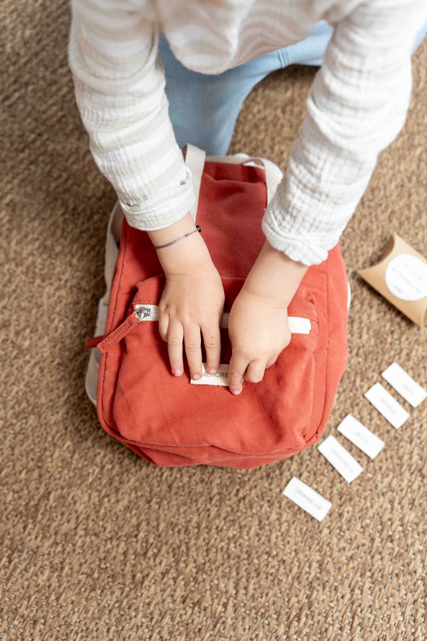 un enfant mettant un scratch sur un sac à dos rouge brique