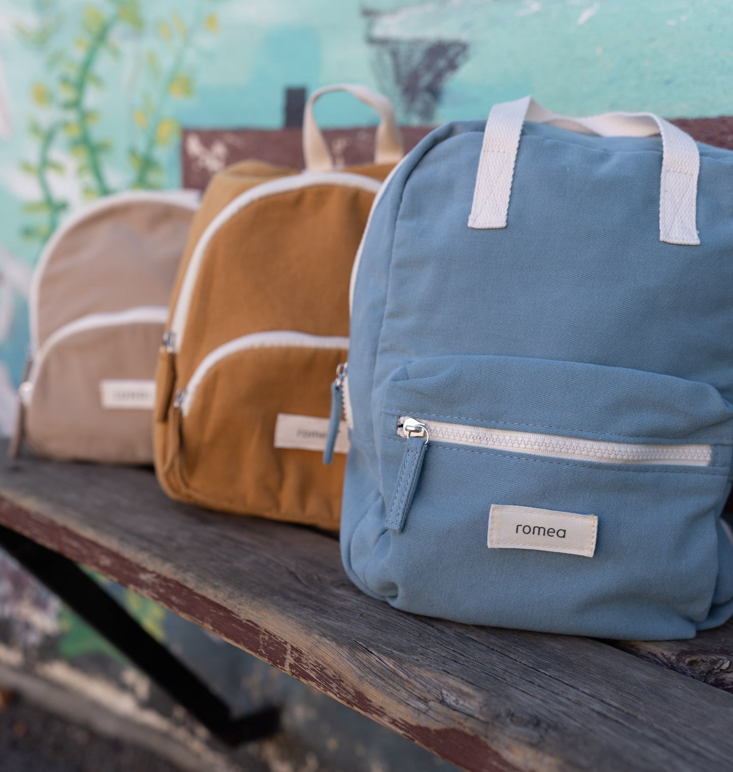 sac de couleur beige, moutarde, et bleu posé sur un banc d'école