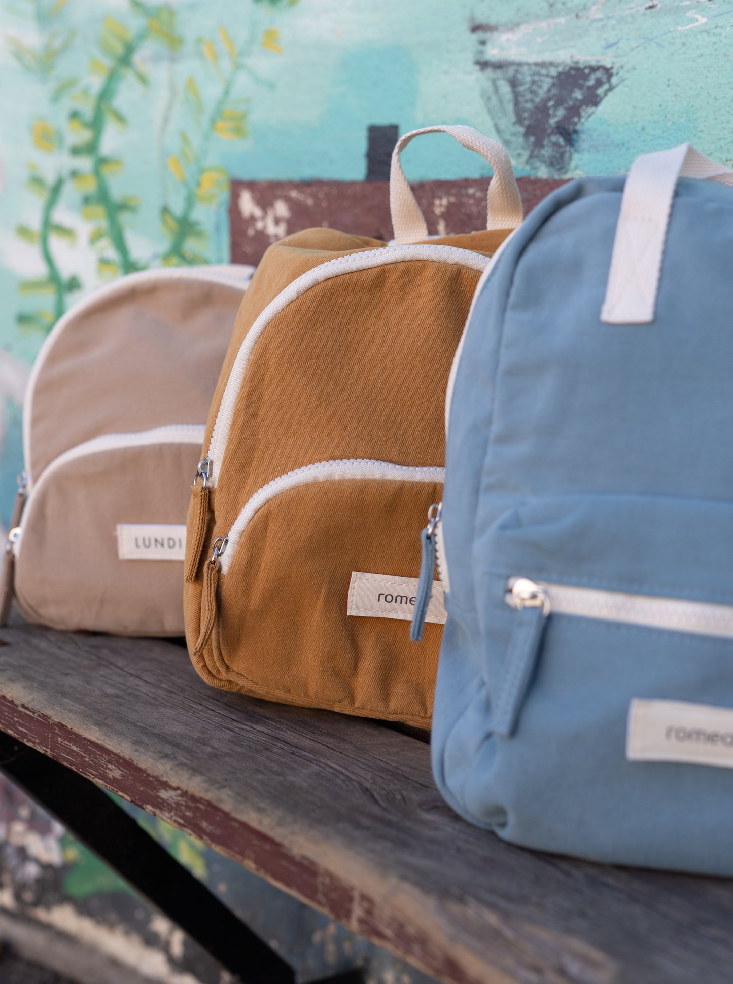 trois sacs de couleur beige, moutarde, bleu posé sur un banc d'école