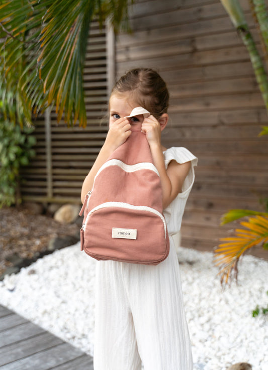 une fille regarde dans la hanse d'un sac à dos de couleur rose