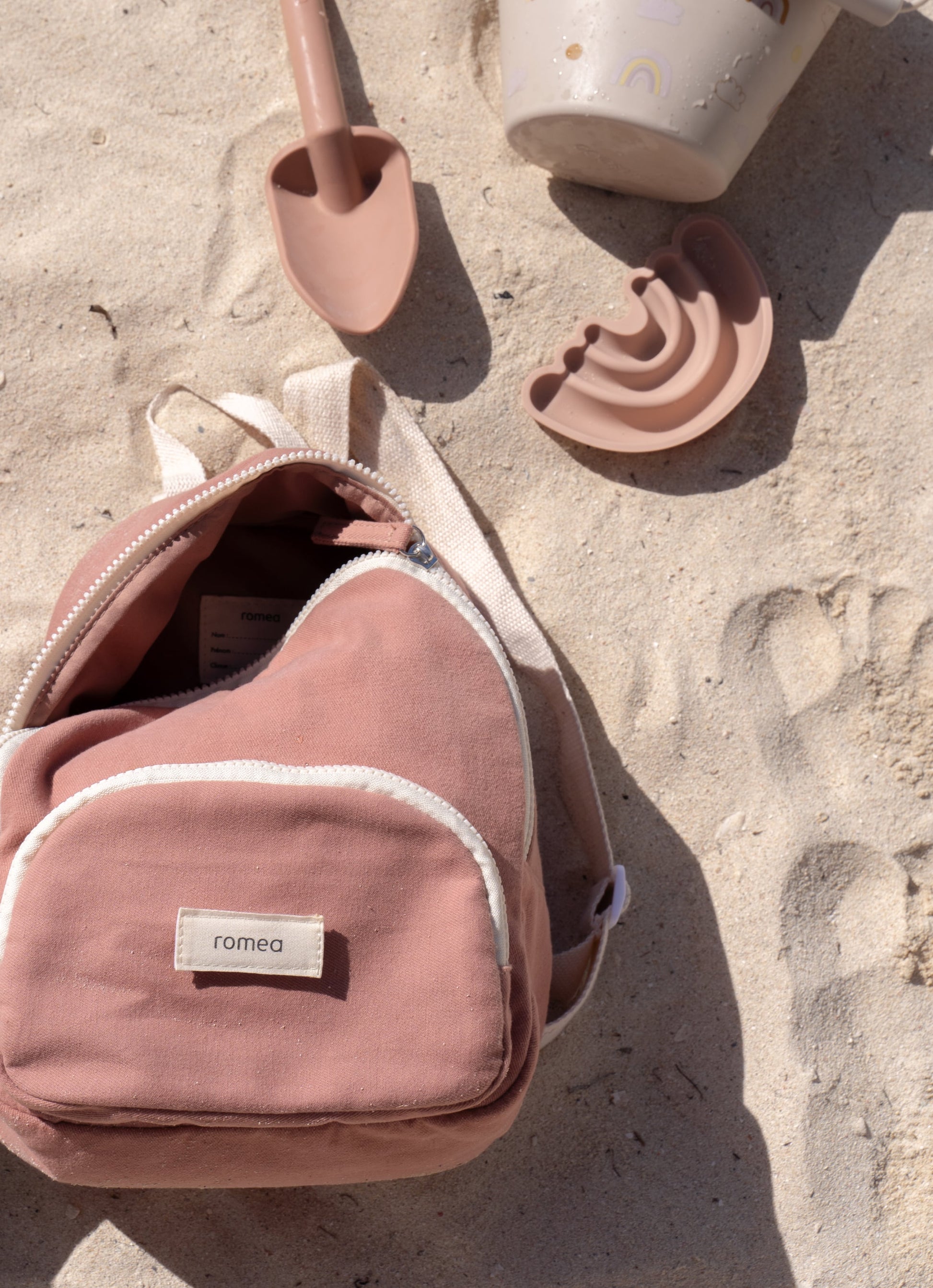 sac à dos de couleur rose posé dans le sable avec des jouets 