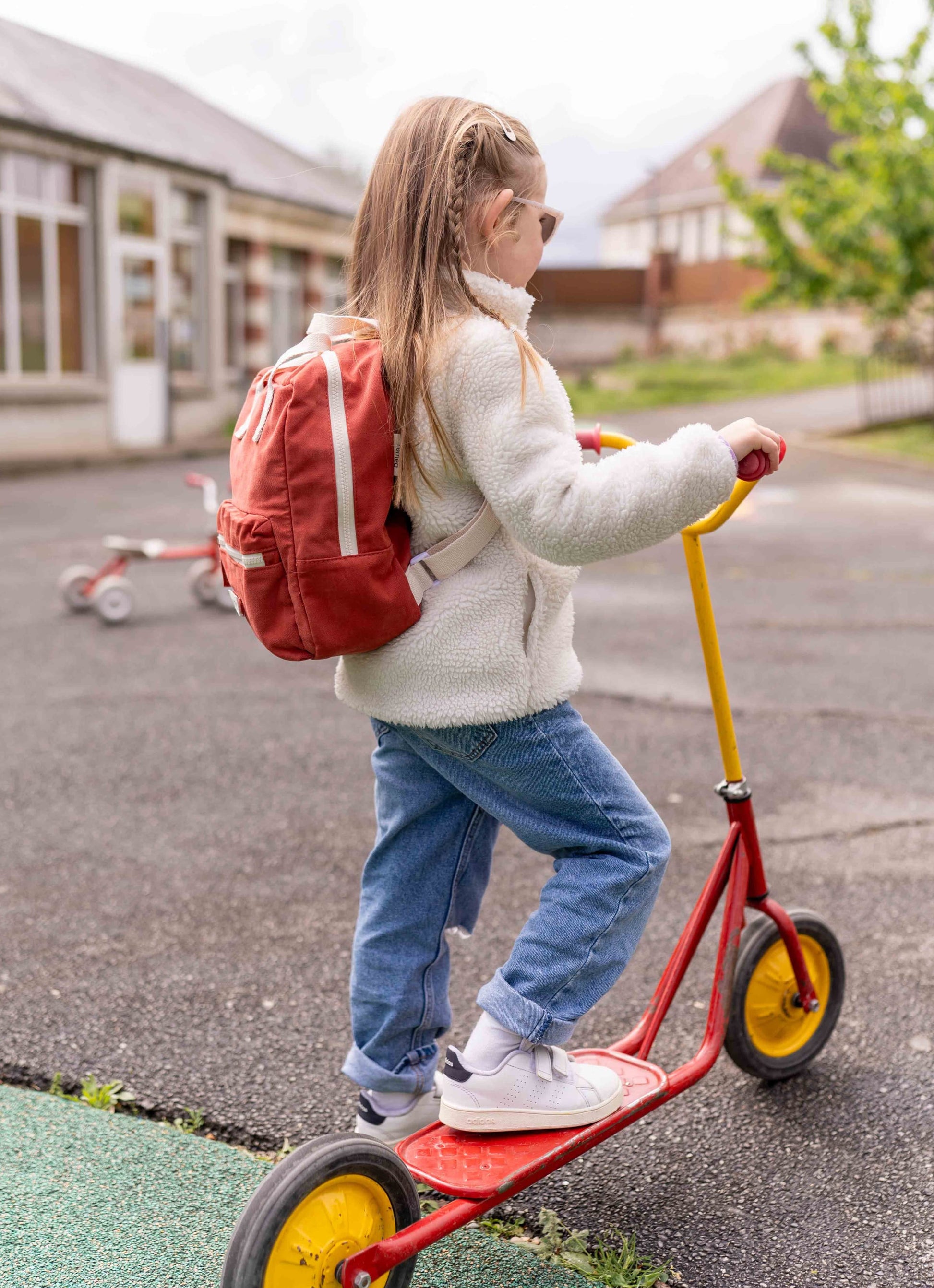 une fille sur une trotinette portant le sac rouge brique 