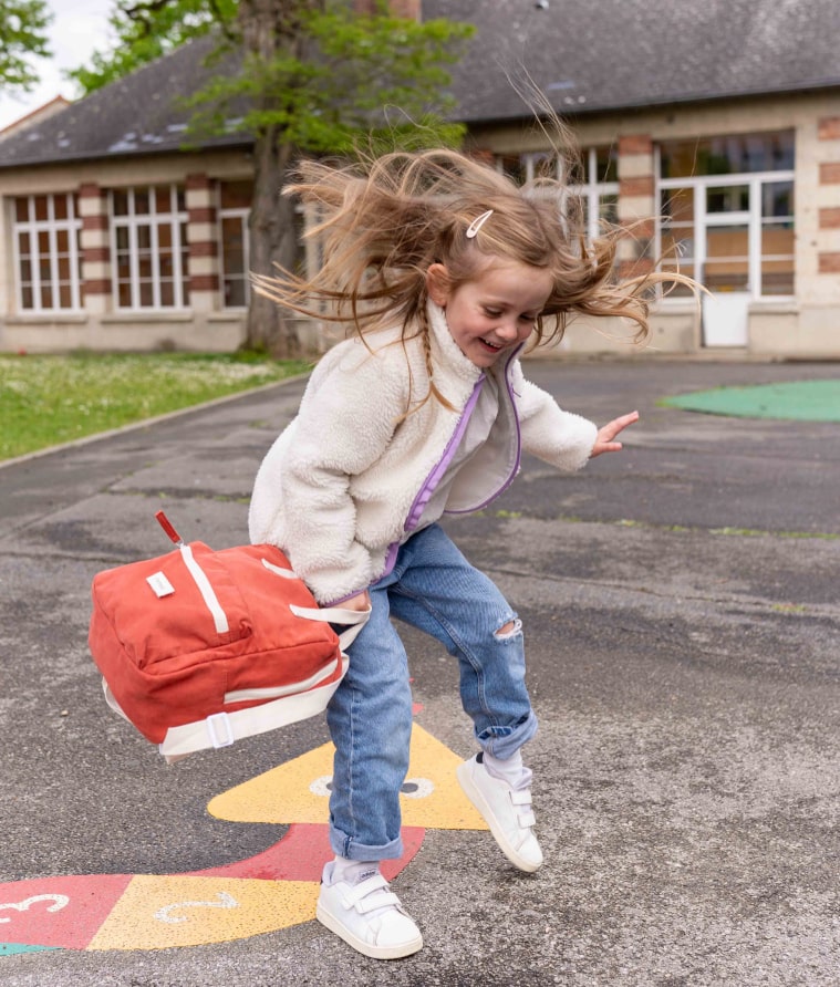 petite fille qui saute avec un sac à dos romea rouge brique 