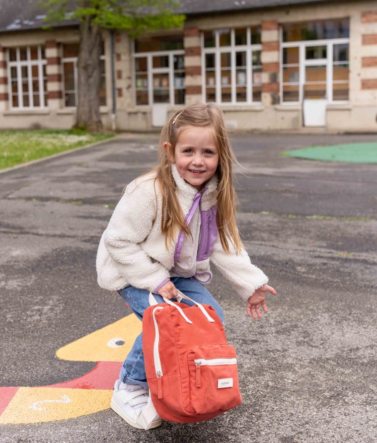 petite fille qui saute avec un sac à dos romea rouge brique 
