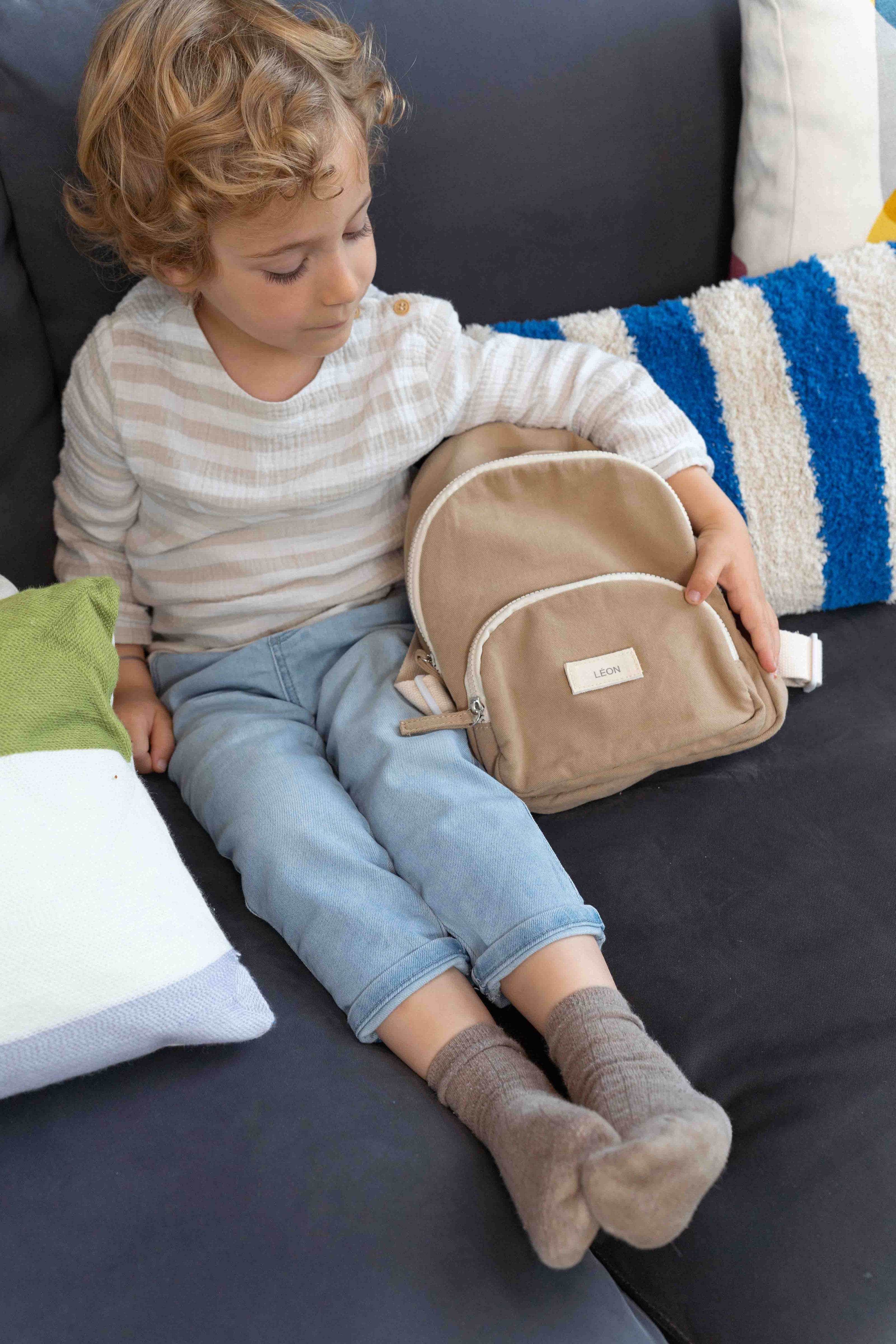 petit garçon assit dans un fauteuil avec un sac à dos de couleur taupe
