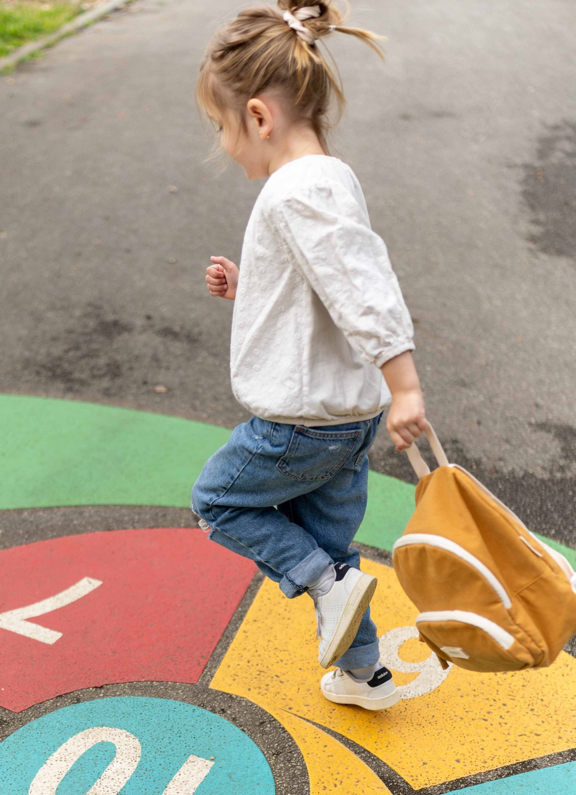 petite fille qui saute avec un sac à dos romea moutarde