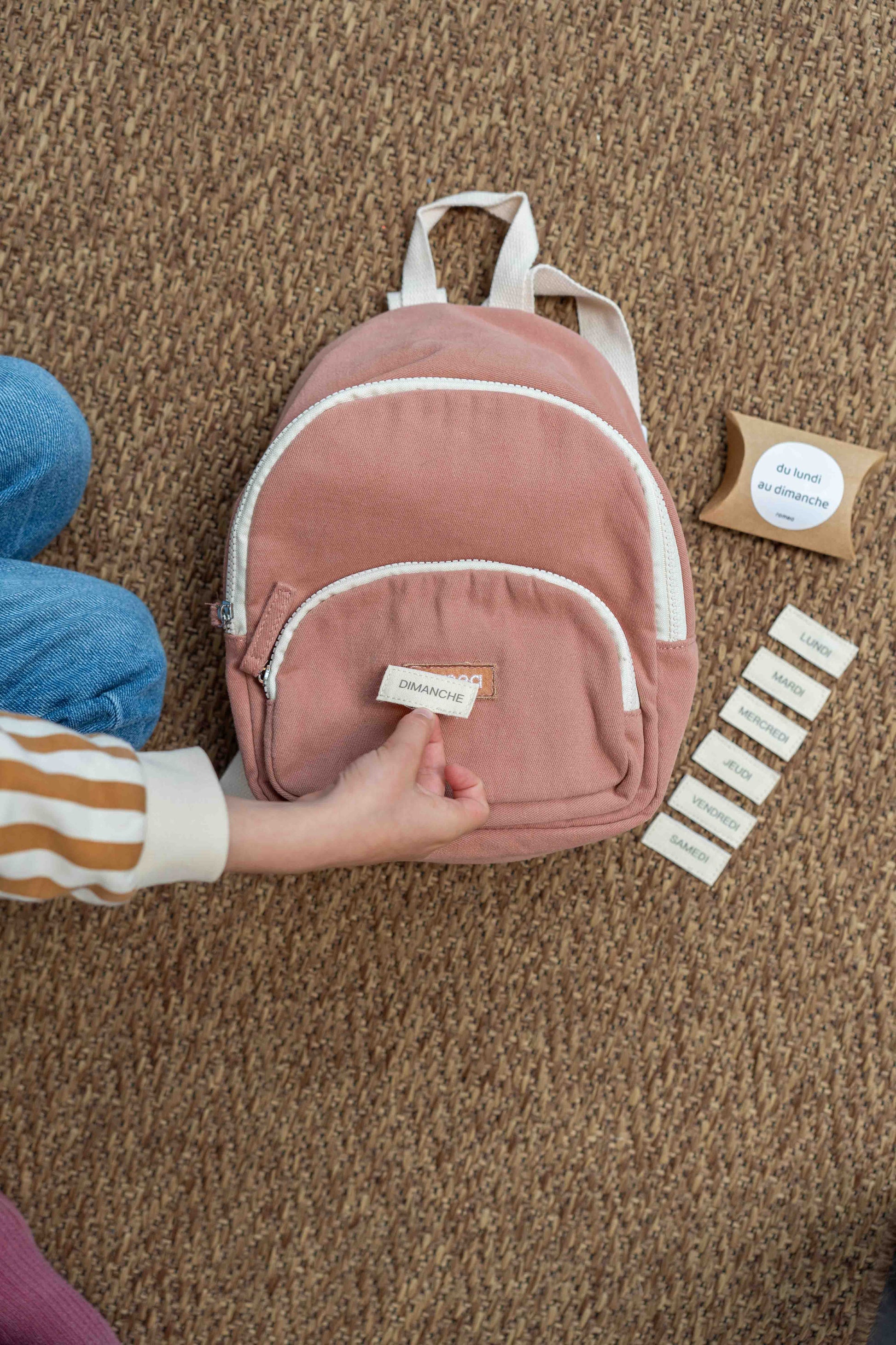 un enfant qui met un kit Scratch jour de la semaine sur un sac de couleur rose poudrée