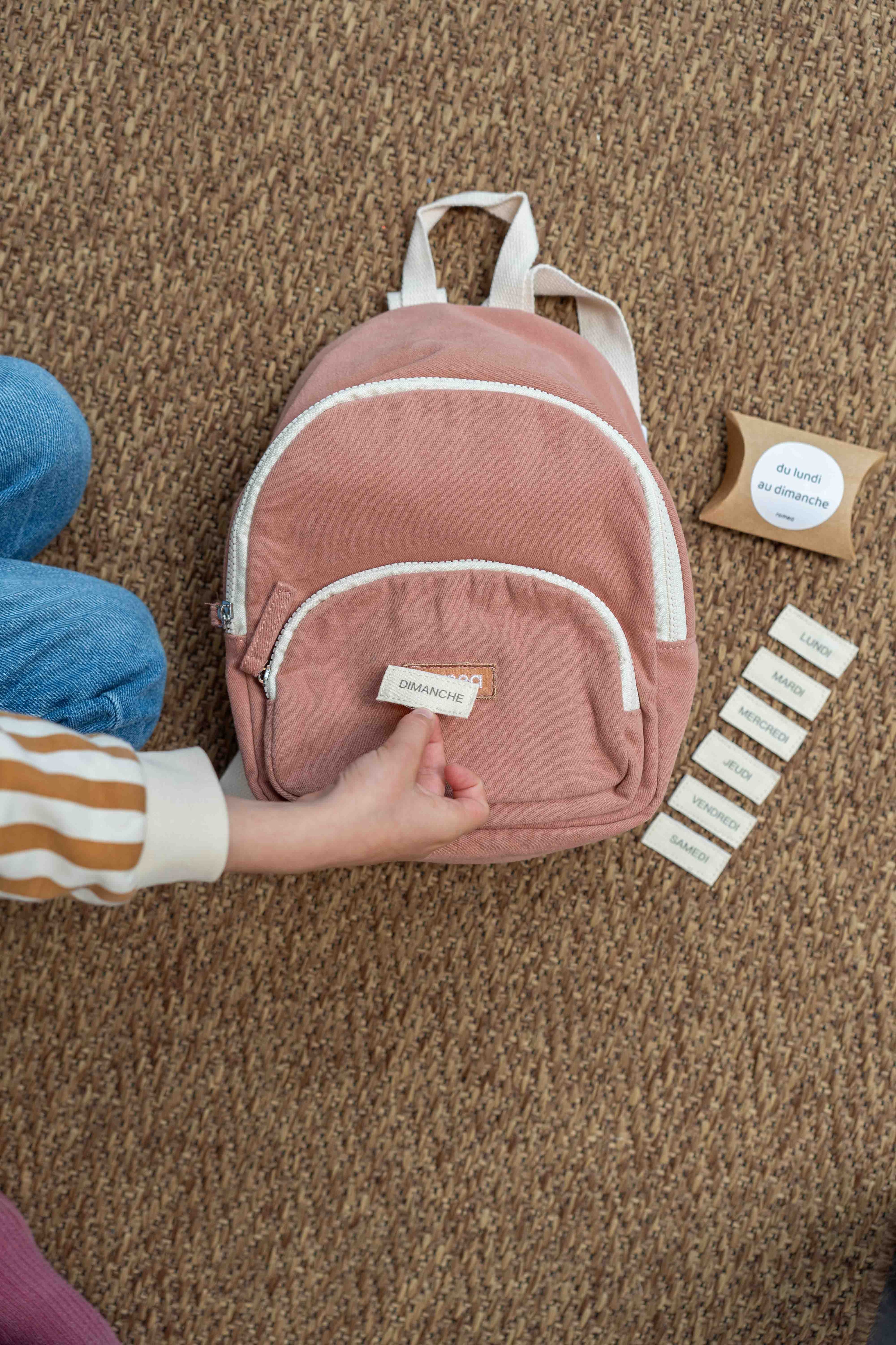 un enfant qui met un kit Scratch jour de la semaine sur un sac de couleur rose poudrée