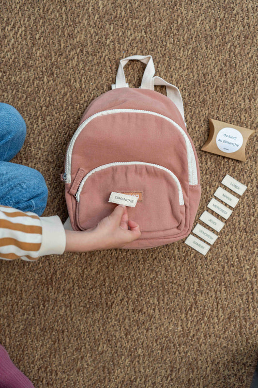 un enfant qui met un kit Scratch jour de la semaine sur un sac de couleur rose poudrée