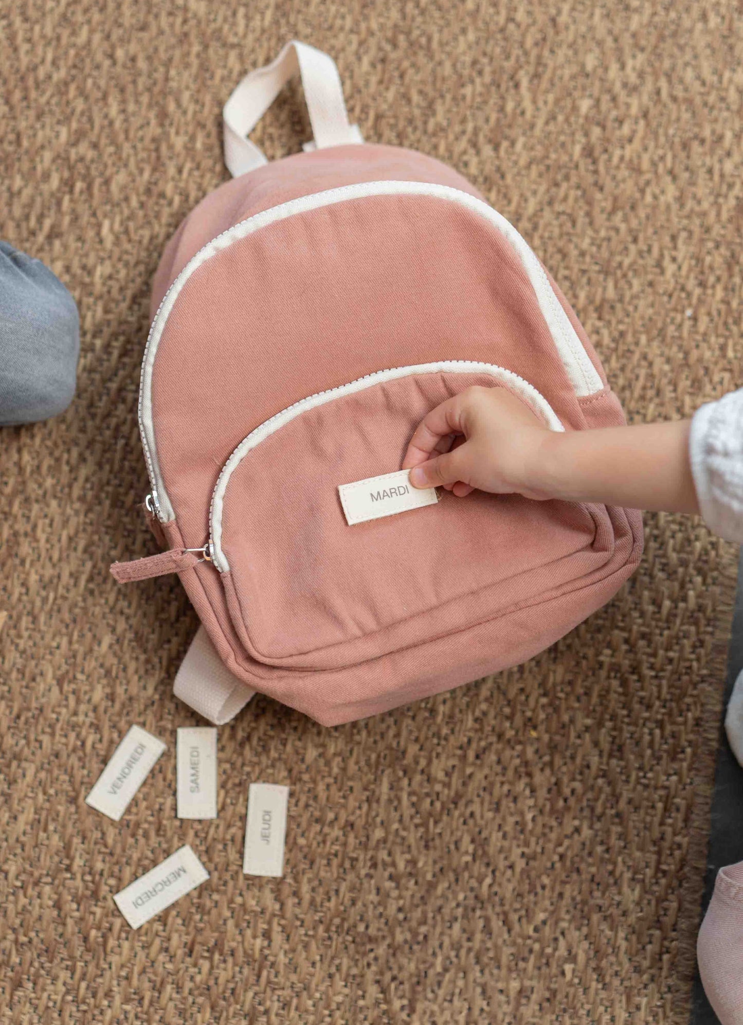 un enfant mettant un scratch sur un sac à dos rose poudrée